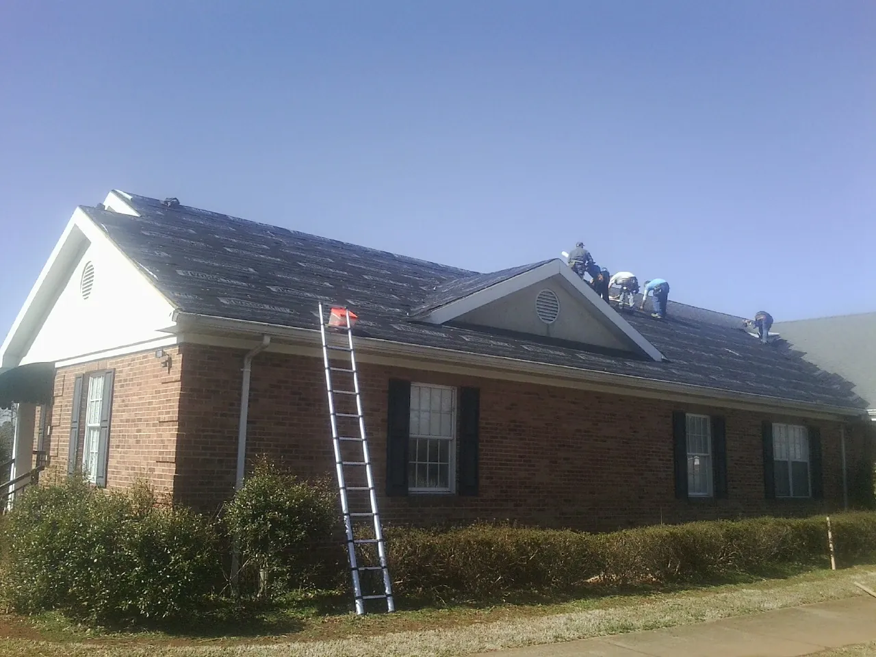 Crew tearing shingles off a brick ranch roof with a ladder set — Emergency Roof Repair work by our crew in Ariel