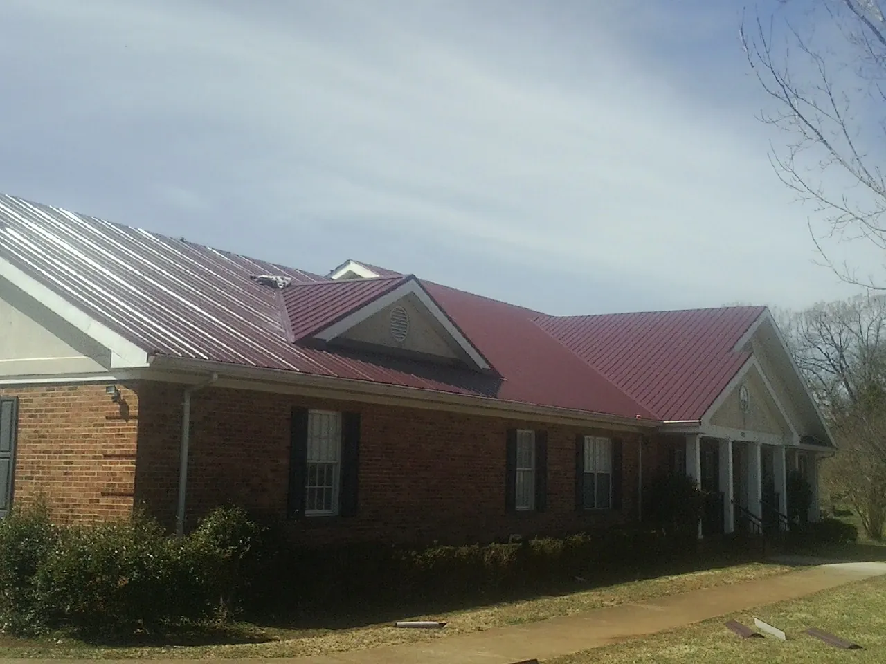 Red metal roof with gabled entries on a long brick building, from a Hail Damage Roof Repair job in Ariel