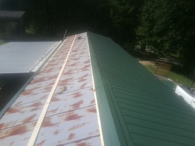 Old rusted panels beside newly installed green metal roofing — Wind Damage Roof Repair by Roofing Brothers in Ariel