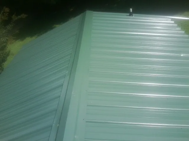 New green metal panels meeting at the ridge of a roof — Flat Roof Repair work by our crew in Ariel