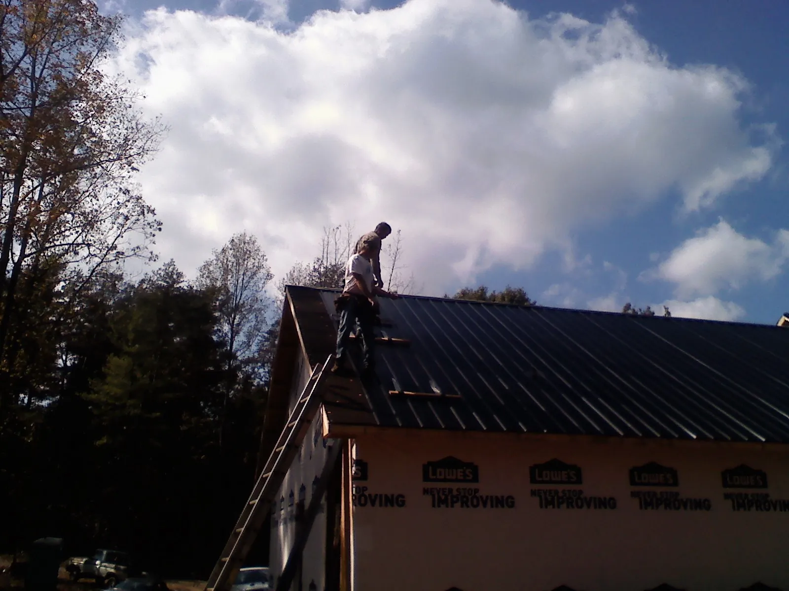 Roofer fastening dark metal panels high against a cloudy sky, from a Roof Inspection job in Ariel