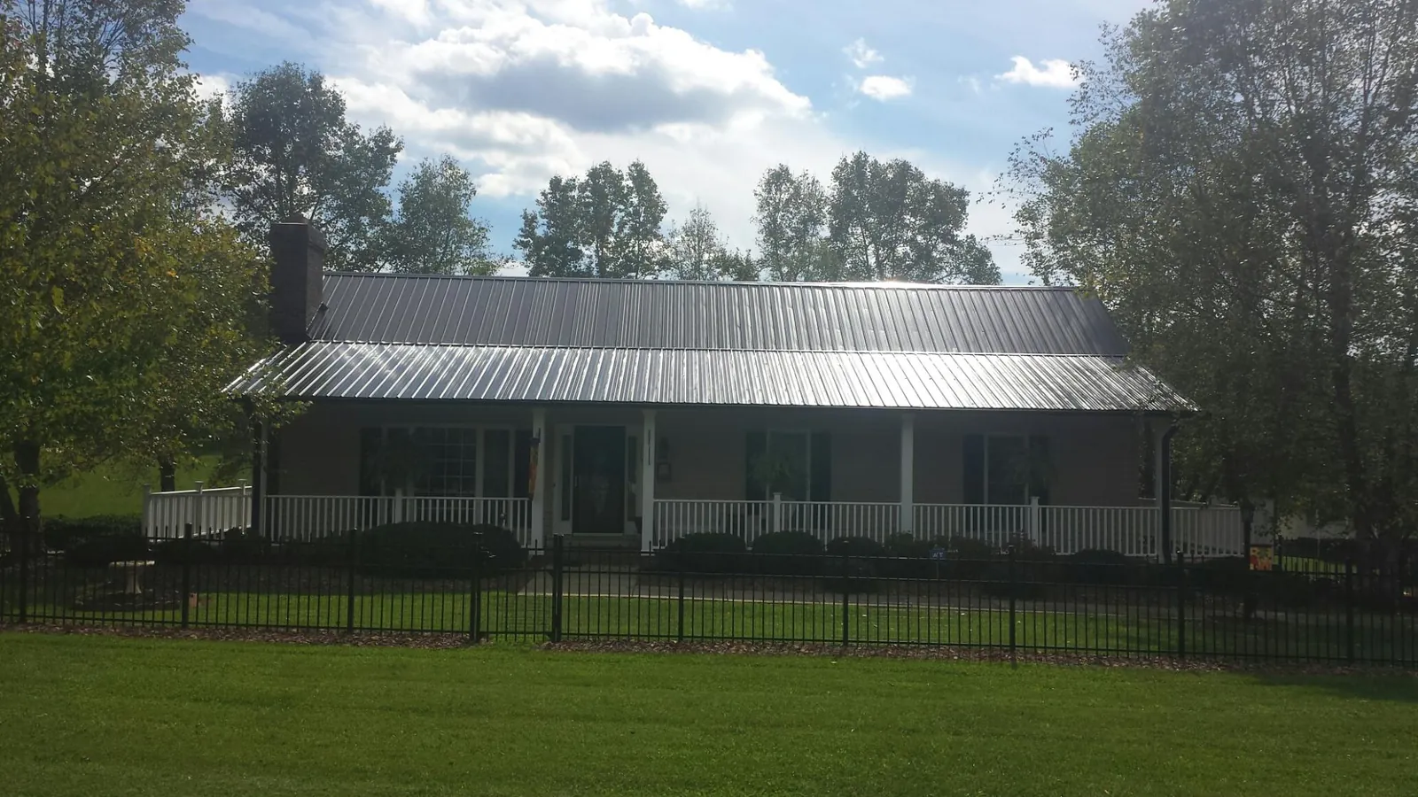 Gray metal roof on a brick ranch with a full width front porch — Gutter Guard Installation work by our crew in Ariel