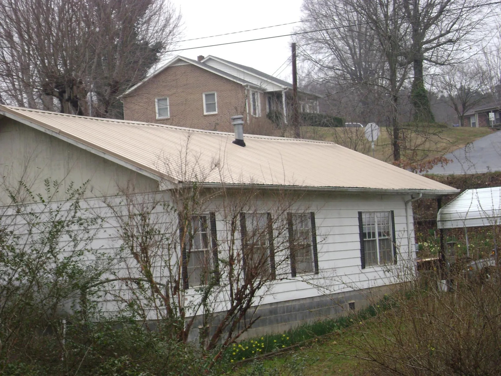 Tan metal roof on a white sided house set into a hillside — Commercial Roofing by Roofing Brothers in Ariel